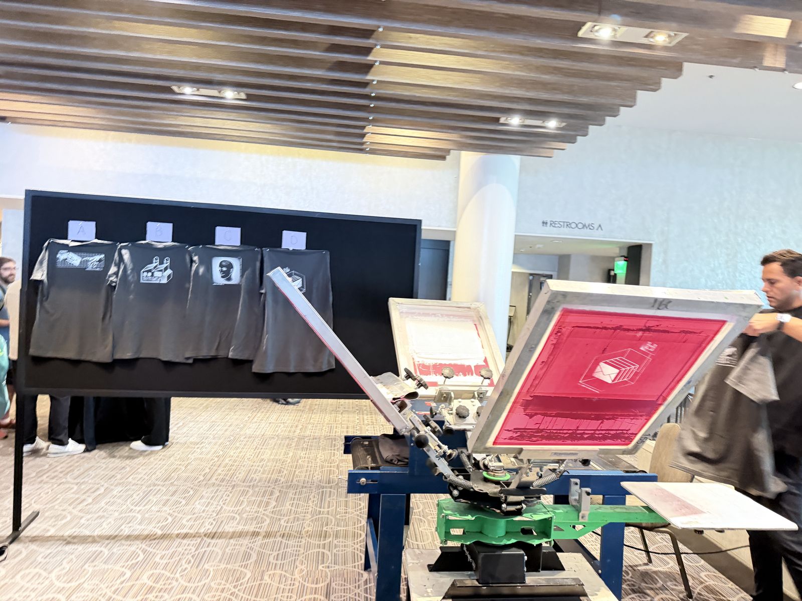 Screen printing carousel set up in a carpeted ballroom foyer with garments on display