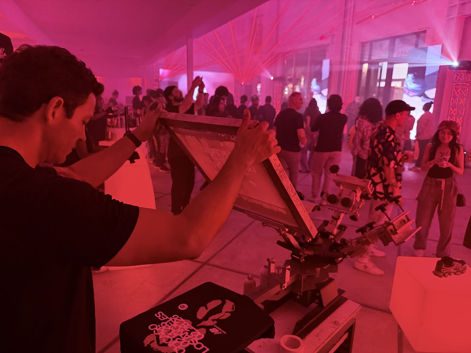 Printer working a manual press under warm red tent lighting at a night event