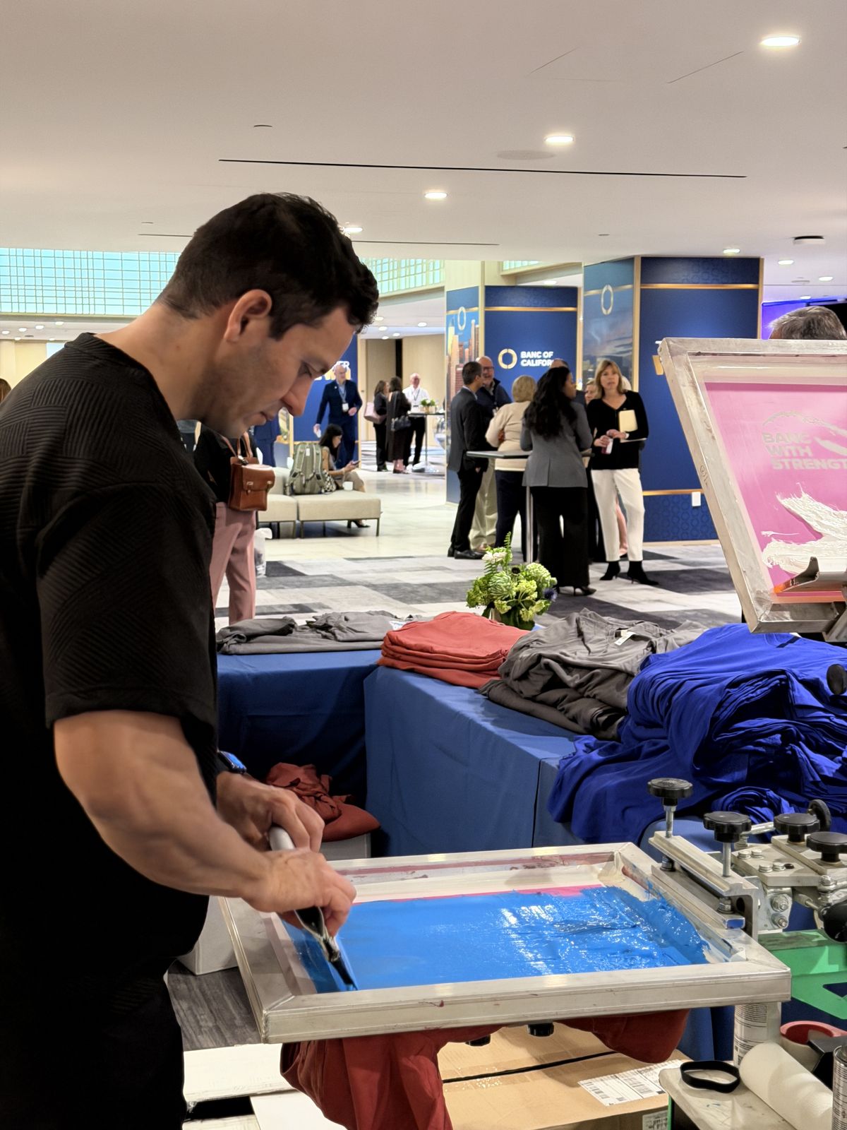 Merch Troop printer pulling a print at a live station with folded apparel staged behind him