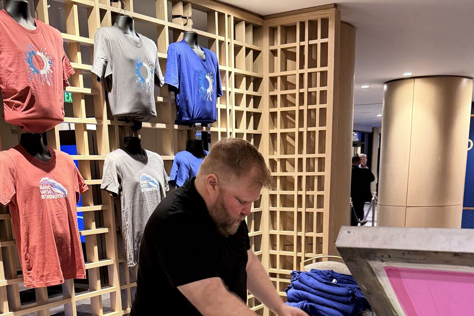 Wall display of printed shirts in multiple colorways beside a working press